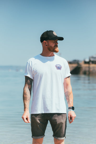 Man wearing the white Queen of Swords graphic T-shirt by Old Elton’s Clothing beside the sea.